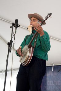 Don Flemons plays the pipes and banjo before a microphone.
